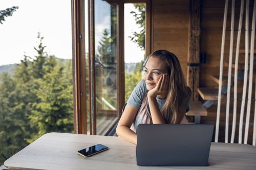 Foto: Junge Frau, die den Blick durch das Fenster einer Blockhütte betrachtet